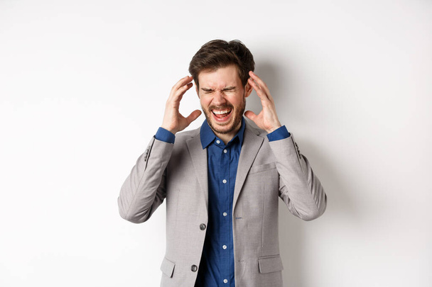Frustrated business man in suit going crazy, screaming and shaking hands near head, feeling annoyed or angry, shouting distressed, standing on white background - Photo, Image