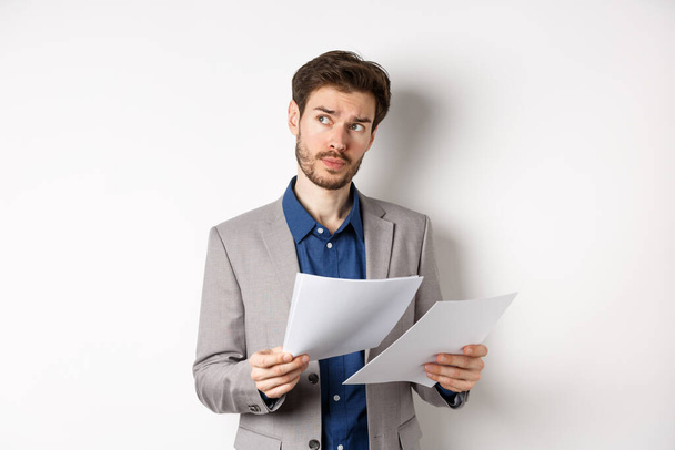 Geschäftsmann im Anzug blättert in Zeitungen, liest Dokumente bei der Arbeit und denkt nach, blickt zur Seite auf das Logo, steht beschäftigt auf weißem Hintergrund - Foto, Bild