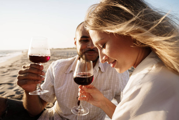 Portrait of a young couple sitting on the beach and drinking wine - Photo, image