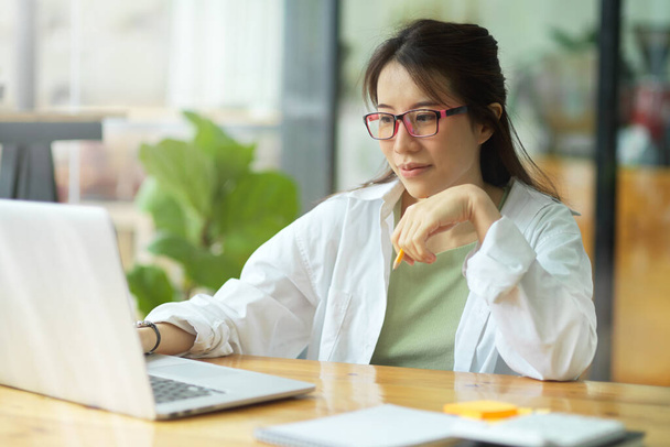 Image d'une jeune femme d'affaires ou d'un étudiant avec des lunettes regardant un ordinateur portable, travaillant sur un ordinateur portable au bureau - Photo, image