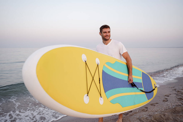 Young man carrying sup board after water surf session - Foto, Imagen