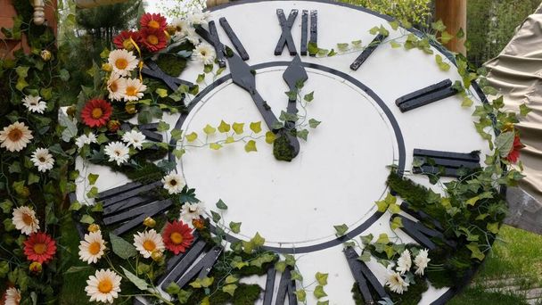 Μεγάλο ρολόι τοίχου στο πεδίο σε ανθισμένα λουλούδια, που δείχνει την ώρα 11: 55, 12: 00. Άνοιξη ή γάμος. Πικνίκ για τις γυναίκες ημέρα - Φωτογραφία, εικόνα