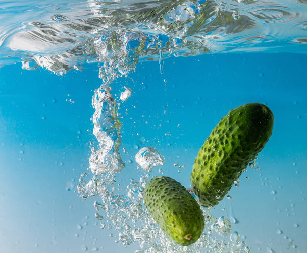 green cucumber falls into the water scattering a lot of sprays and drops. - Photo, Image