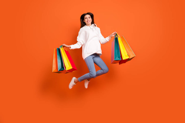 Full length body size view of attractive cheerful girl jumping carrying bags outlet offer isolated over bright orange color background - Valokuva, kuva