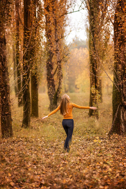 Девушка гуляет по осеннему лесу. Молодая женщина крутится на фоне апельсиновых деревьев.. - Фото, изображение