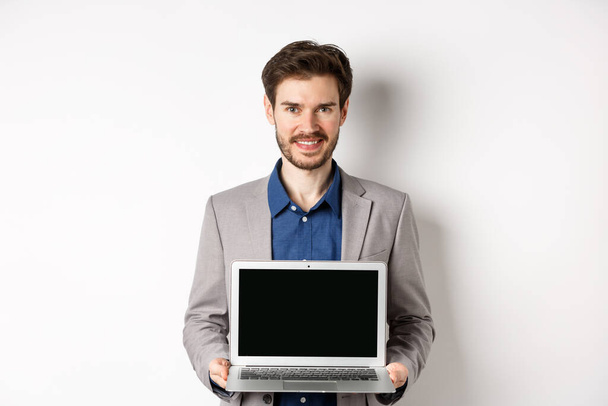 Handsome caucasian businessman in suit showing empty laptop screen, demonstrate promo, standing on white background - Photo, Image