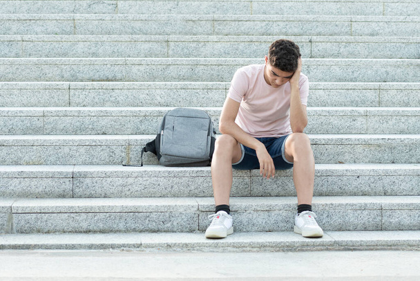 Droevige en gefrustreerde Spaanse tiener die op de trap zit en zijn hoofd vasthoudt. Angst en depressie in adolescentie concept. - Foto, afbeelding