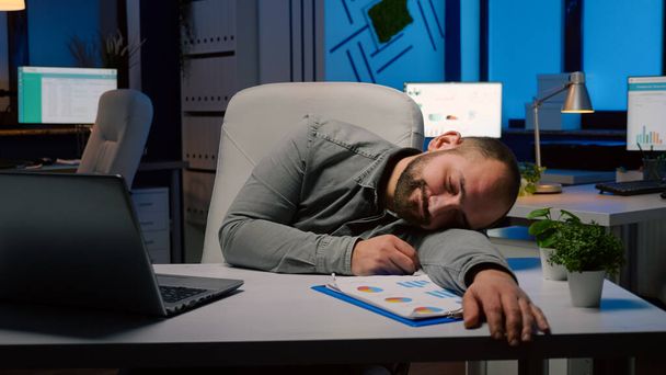 Изможденный перегруженный работой бизнесмен спит на столе в офисе стартапа - Фото, изображение
