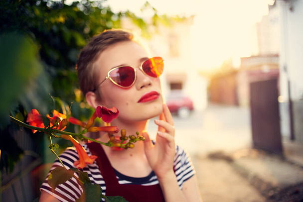 όμορφη γυναίκα φορώντας γυαλιά ηλίου σε εξωτερικούς χώρους μόδας ποζάροντας λουλούδια - Φωτογραφία, εικόνα