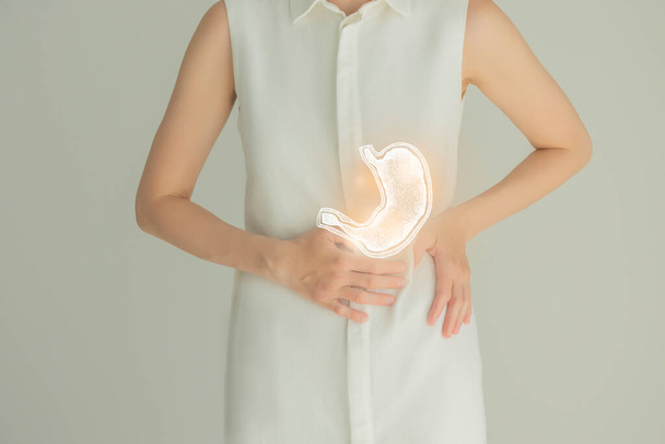 Невпізнавана пацієнтка-жінка в білому одязі, підсвічена ручним шлунком в руках. Концепція проблеми травної системи людини
. - Фото, зображення