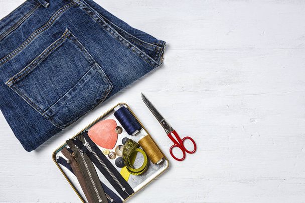 Handicraft, clothing repair. Ripped blue jeans sewing accessories from above. Flat lay - Zdjęcie, obraz
