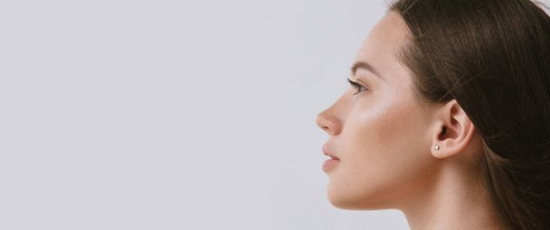 Retrato de cerca de una hermosa hembra con maquillaje natural sobre fondo gris. Vista lateral - Foto, Imagen