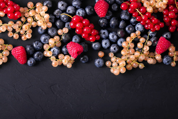 Свіжі літні ягоди в старовинному кубку на чорному тлі, вид зверху
 - Фото, зображення