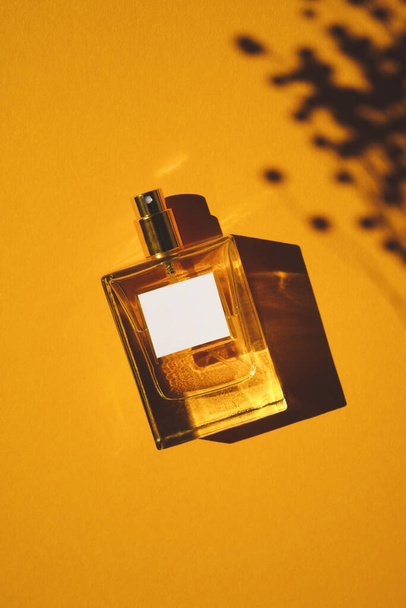 オレンジの背景に透明ボトルの香水。昼の香りのプレゼンテーション - 写真・画像