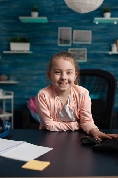 Radosna dziewczynka uśmiecha się siedząc przy biurku do szkoły online - Zdjęcie, obraz