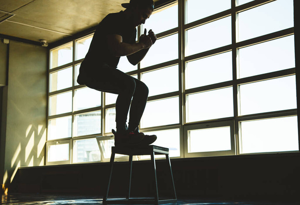 sportman springt op een speciaal platform in de sportschool tegenover het raam. Crossfit silhouet opname - Foto, afbeelding