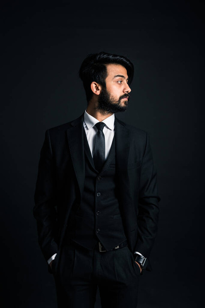 Portrait of a young handsome successful Indian in a classic black three-piece business suit on a dark background - Fotó, kép