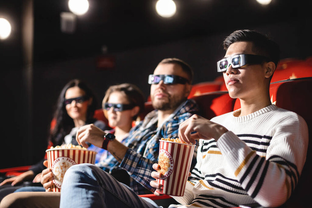Friends are watching a movie in the cinema. People sit in the armchairs of the cinema and look at the screen with special glasses for 3D - Foto, Imagem