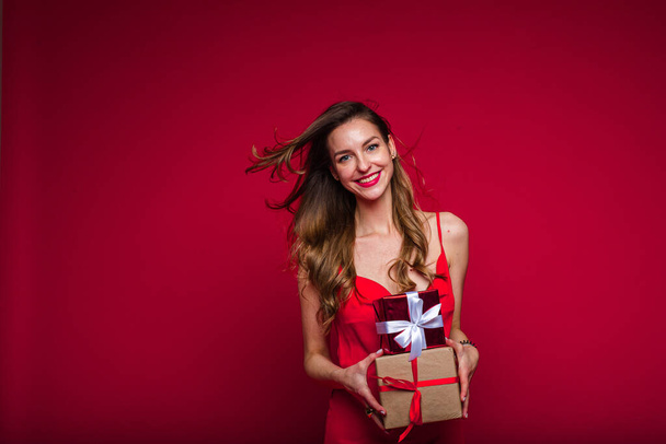 赤いドレスの美しい女性ファッションモデルはプレゼントや喜びを持つ小さな箱をたくさん持っています - 写真・画像