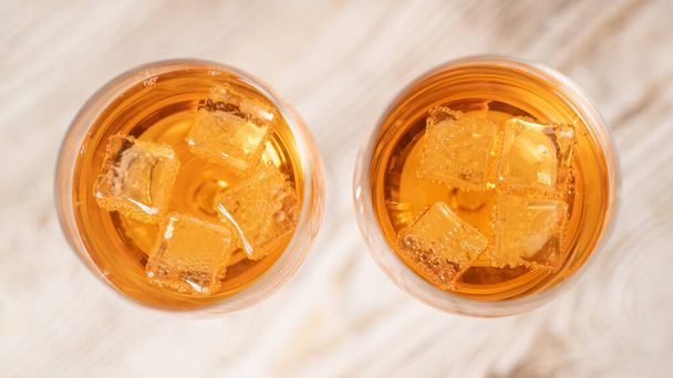 Top view of two glasses of orange cocktails with ice on a wooden table. Ice melting in a cocktail glass - Photo, Image