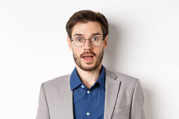 Close-up of surprised business man in glasses and suit gasping amazed, hear good news, standing on white background - Fotó, kép
