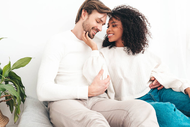 Smiling beautiful woman and her handsome boyfriend. Happy cheerful multiracial family having tender moments. Multiethnic models lying in bed and hugging in white interior. Embracing each other - Photo, image