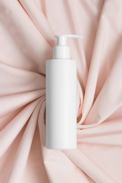 White cosmetic shampoo dispenser bottle mockup on the soft pink textile. - Fotó, kép