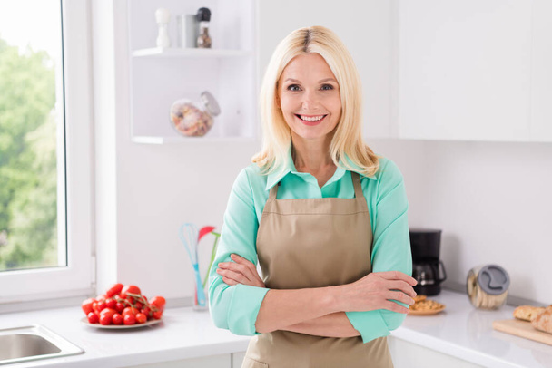 Foto de mujer madura feliz sonrisa positiva cruzada manos confianza usar delantal cocinero cocina cocina interior - Foto, imagen