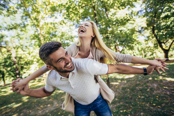 Boyfriend carrying his girlfriend on piggyback in autumn park. - Фото, изображение