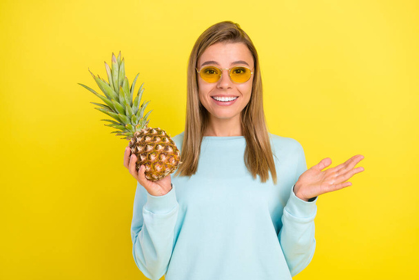 Photo of charming blonde lady hold fresh pineapple beaming smile wear sunglass blue shirt isolated on yellow background - Valokuva, kuva