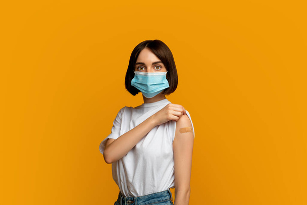 Vaccination and immunization concept. Lady wearing protective mask and showing plaster on shoulder after injection - Foto, Imagen