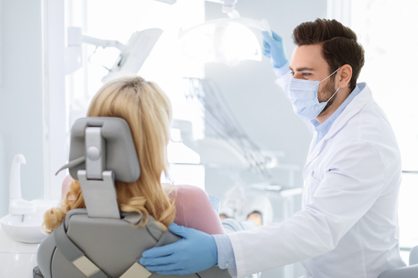 Dentiste masculin en masque visage saluant femme blonde patiente - Photo, image