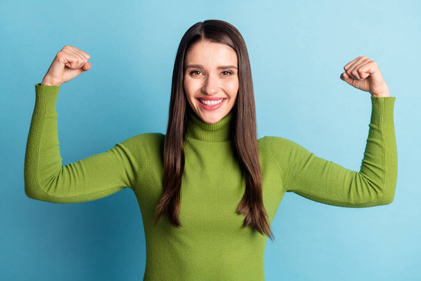 Photo of positive lovely cute lady hands showing biceps wear green turtleneck isolated on blue background - Fotó, kép