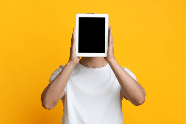 Nierozpoznawalny facet chowający się za cyfrowym tabletem z pustym ekranem - Zdjęcie, obraz