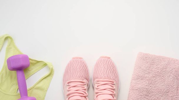 un par de zapatillas de deporte de color rosa, una toalla de rizo y una mancuerna de plástico sobre un fondo blanco, vista superior, espacio para copiar - Foto, imagen