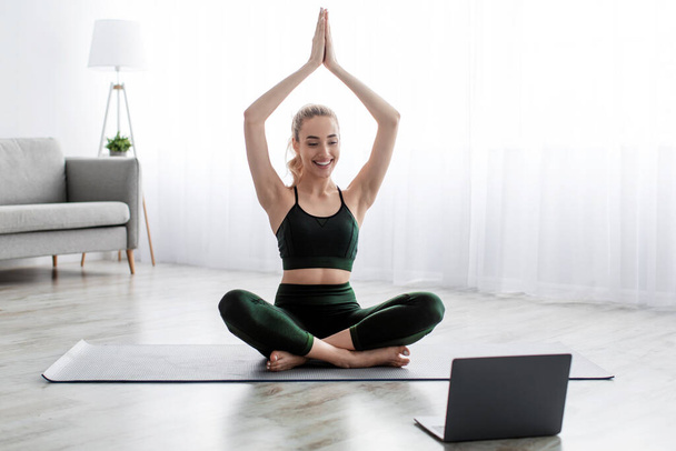 Satisfied caucasian beautiful young blonde woman practicing yoga in lotus position, exercising at home - Fotó, kép