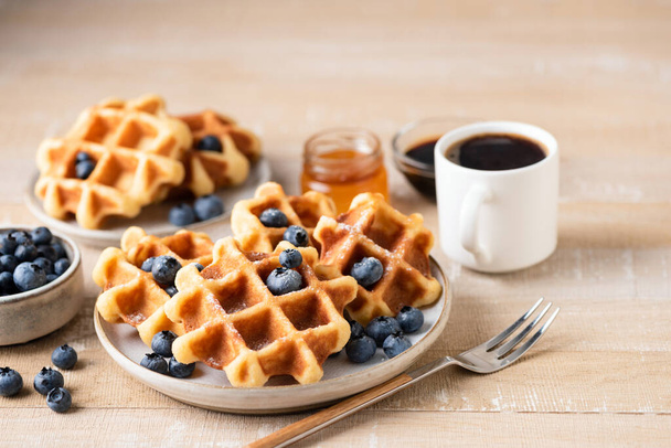 Belgian waffles with blueberries and a cup of black coffee on wooden table, breakfast in cafe - Foto, afbeelding