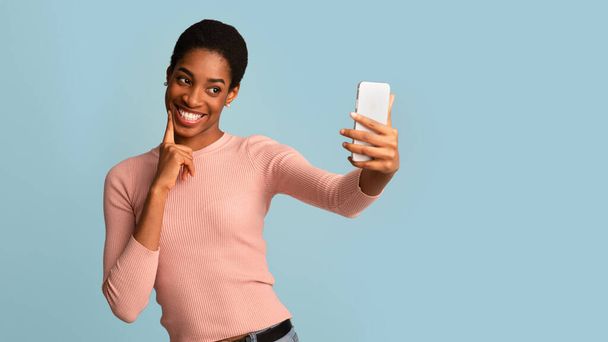 Милая молодая черная женщина делает селфи на смартфоне, улыбается на камеру устройства - Фото, изображение