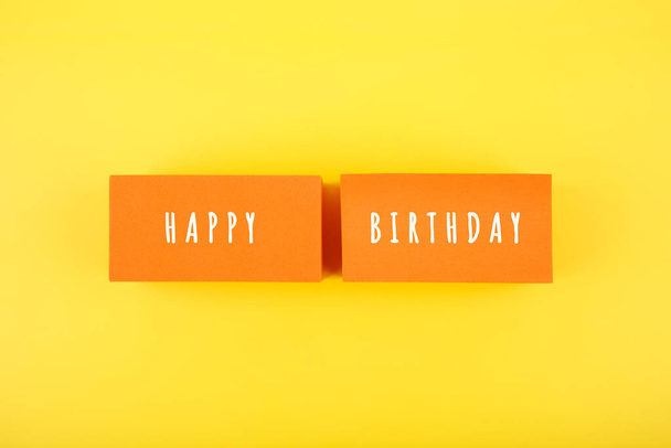 Happy Birthday bright fun colorful concept on yellow background. Happy Birthday written on orange tablets against yellow background - Fotografie, Obrázek