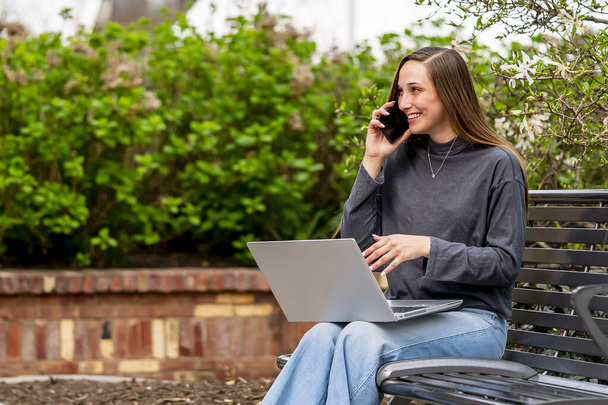 A gorgeous brunette model works on her computer outdoors while enjoying the spring weather - Φωτογραφία, εικόνα