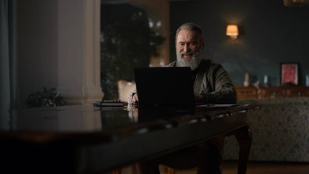 Старый бизнесмен закрывает ноутбук в домашнем офисе. Работа по отделке - Фото, изображение