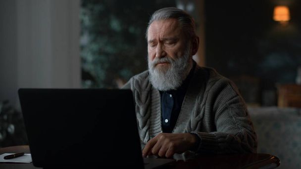 Сосредоточенный старший мужчина разговаривает во время видеозвонка на ноутбуке - Фото, изображение