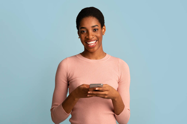 Σπουδαία εφαρμογή. Πορτρέτο της χαρούμενης νεαρής μαύρης γυναίκας με Smartphone στα χέρια - Φωτογραφία, εικόνα