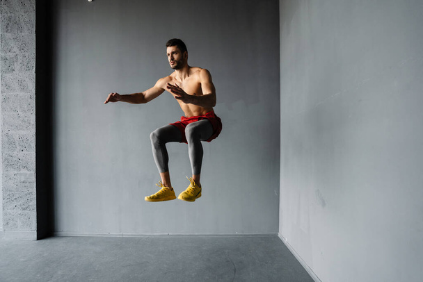 Young fit muscular shirtless sportsman jumping exercising indoors - Photo, Image