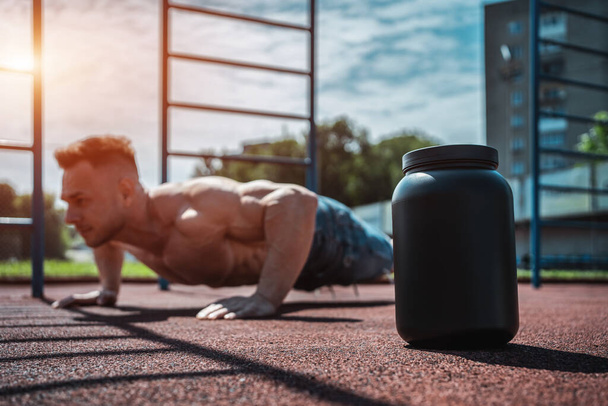 protein whey drink in black container and muscular athlete exercising outdoor - Fotografie, Obrázek
