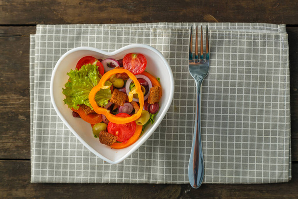 Vegetable salad in a heart shape plate on a wooden table on a napkin. Horizontal photo - Foto, imagen