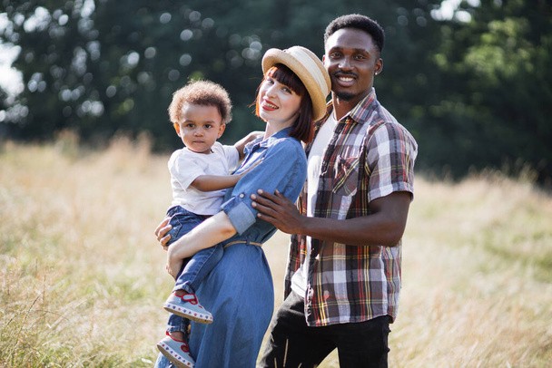 Multi ethnic parents with son on hands posing on summerfield - Fotoğraf, Görsel