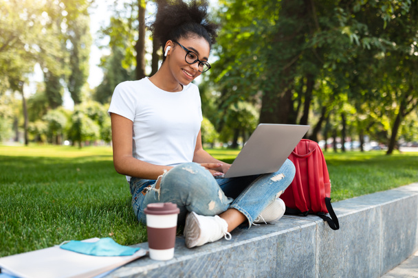 Estudiante negro feliz viendo la conferencia en el ordenador portátil en el parque, Vista lateral - Foto, Imagen