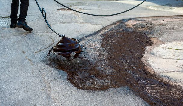 Emulsión del betún de pulverización del trabajador del camino con la lanza de pulverización manual antes de aplicar una nueva capa de asfalto - Foto, imagen