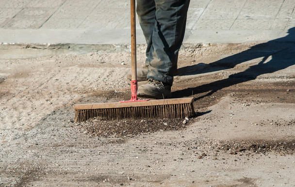 worker with large scrub brush collect residues of asphalt milling - Photo, Image